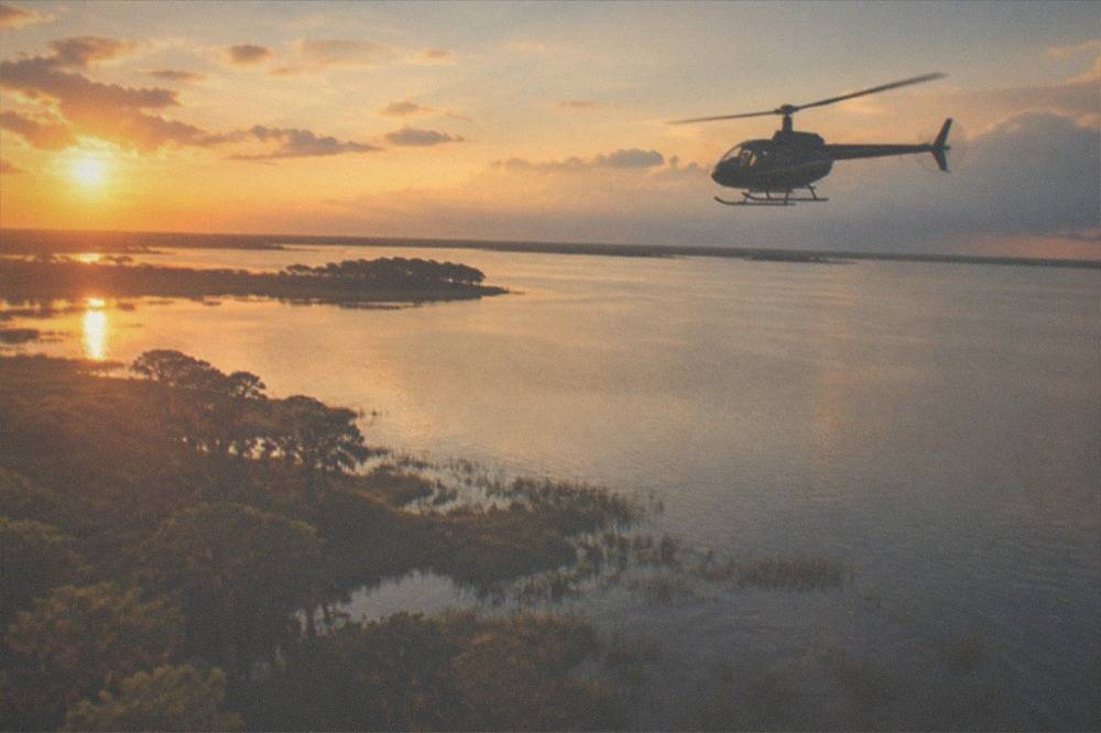 A tour helicopter cruising above Florida lakes and resort buildings at golden hour