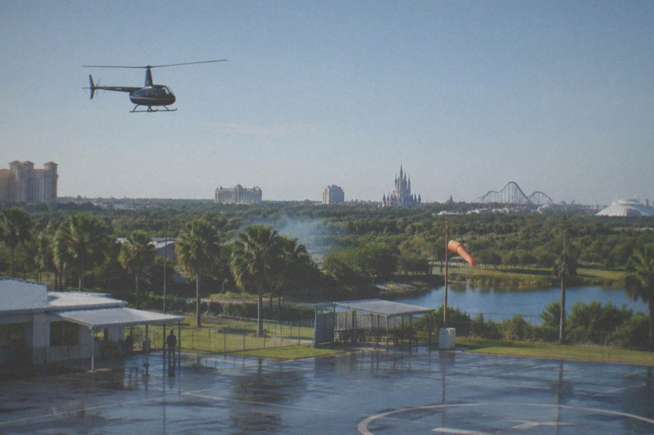 A small sightseeing helicopter flying above the Orlando theme park corridor on a clear afternoon