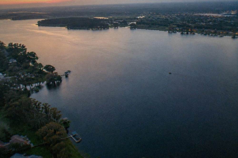 An aerial view of a wide Florida lake with tree lines and distant development at dusk