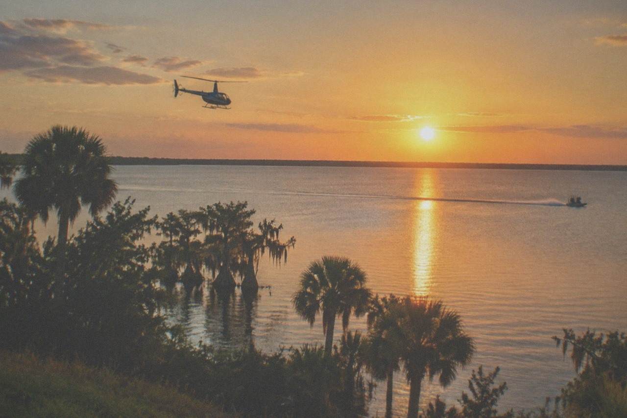 A small sightseeing helicopter flying over a calm Florida lake at golden hour
