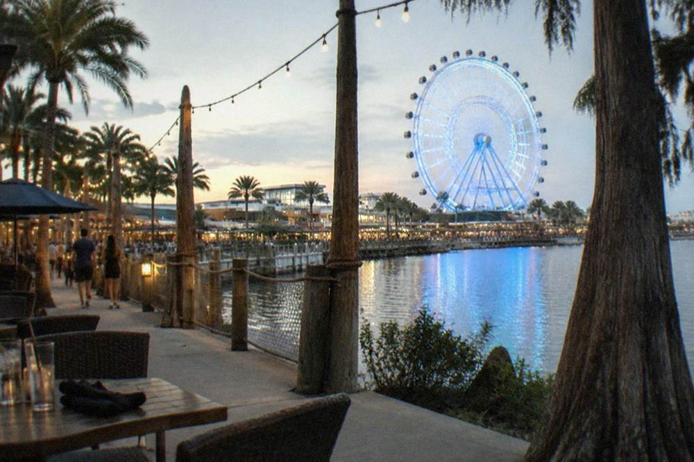 A waterfront walkway with string lights and restaurant patios in the evening