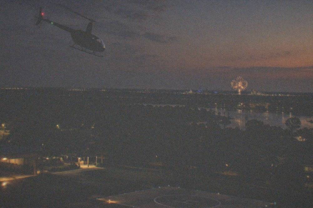 A helicopter flying above city lights with fireworks glowing on the horizon
