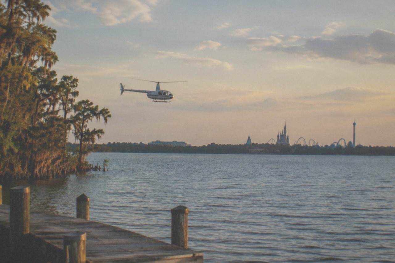 A helicopter flying over Central Florida lakes and theme park towers in warm late afternoon light