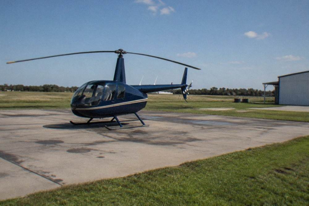 A tour helicopter on a paved helipad with rotor blades stationary and open sky above