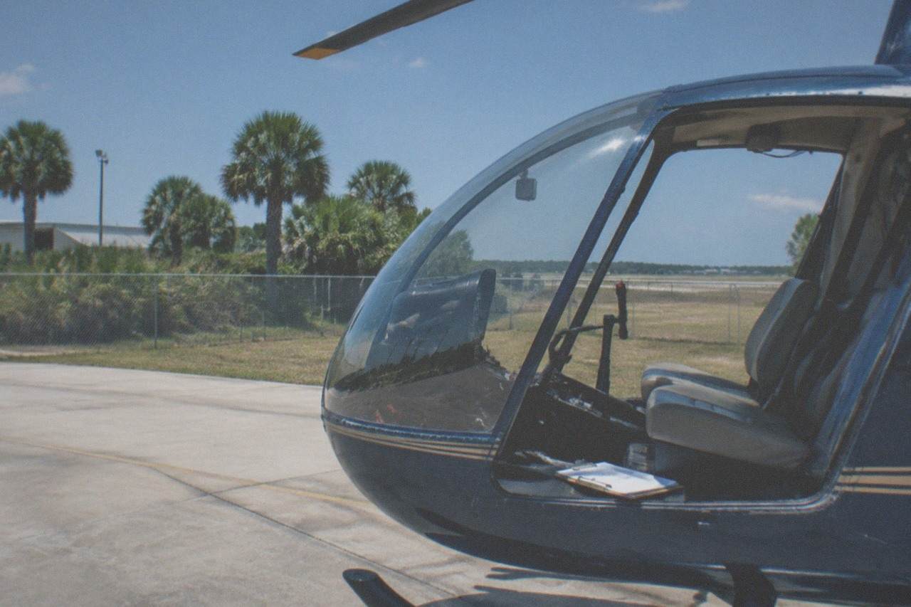A small sightseeing helicopter parked on a sunny Kissimmee helipad with palm trees in the background