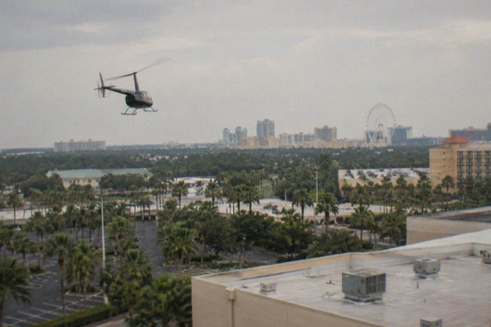 Small tour helicopter climbing above a Florida resort corridor with palm trees and parking lots below