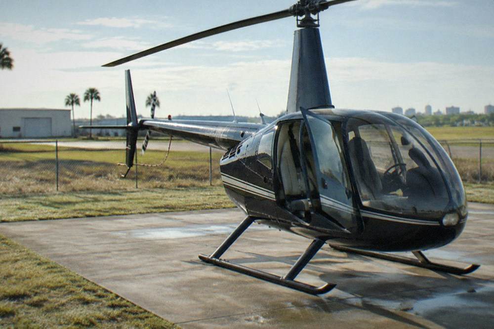 Robinson tour helicopter parked on a Kissimmee helipad with rotor blades stopped and open doors