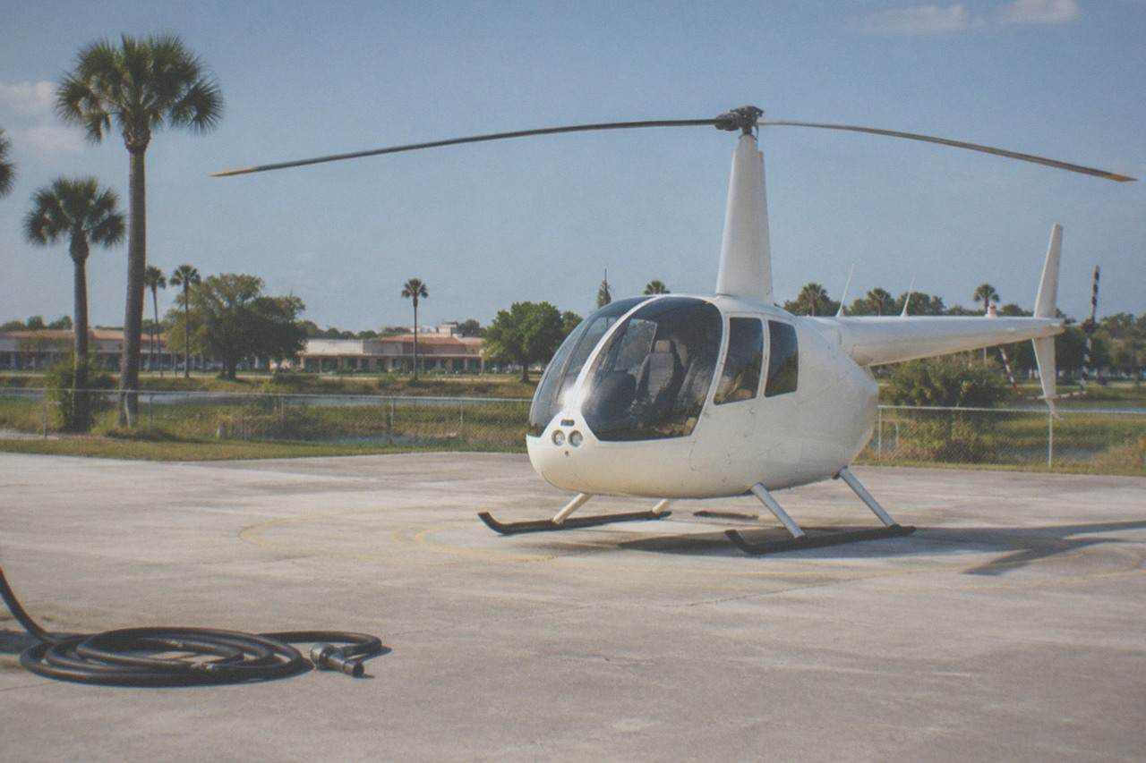 Light helicopter on a paved helipad beside a Florida tour corridor at midday