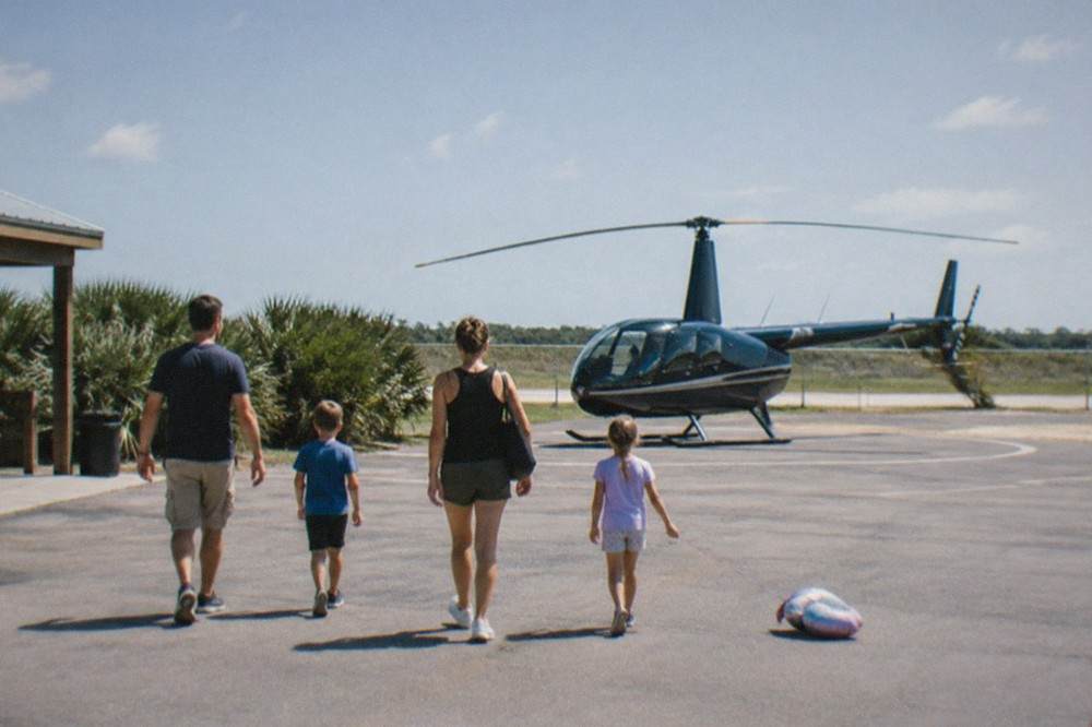 A family walking toward a small helicopter on a sunny Kissimmee helipad