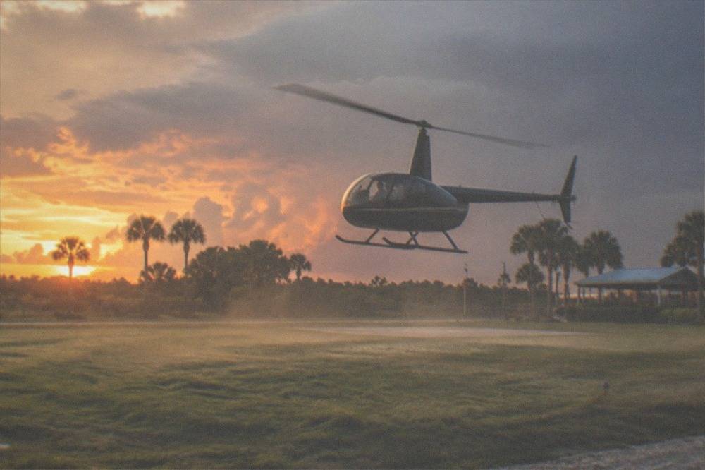 A tour helicopter lifting off from a grassy helipad near Kissimmee at golden hour