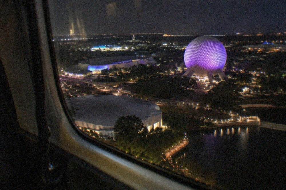 A couple's view from a helicopter window at night with theme park lights spread across the horizon