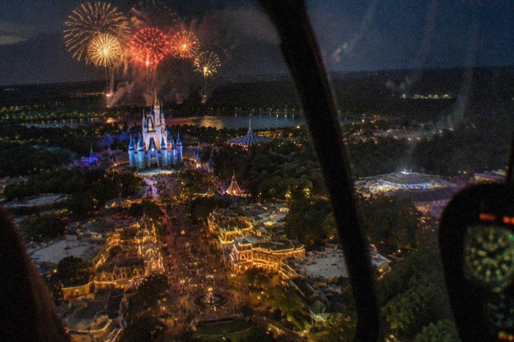 Theme park fireworks bursting above the horizon as seen from above the tree line at night
