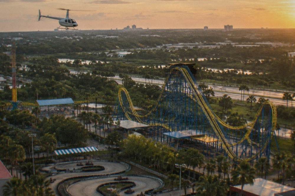 Helicopter flying above a small amusement park with roller coasters and go kart tracks below