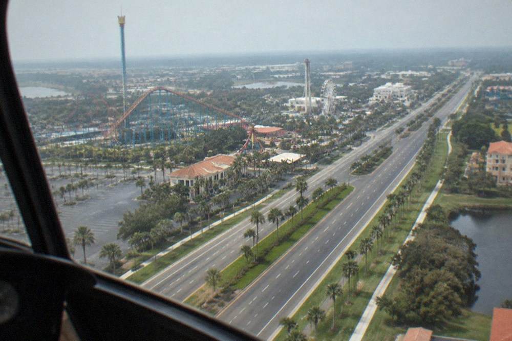 View from a helicopter window over a highway corridor with amusement park rides in the distance