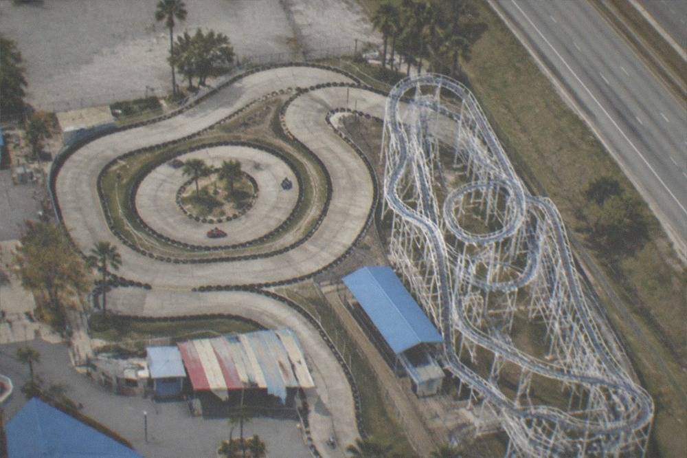 Amusement park roller coasters and go kart tracks seen from above beside a wide road