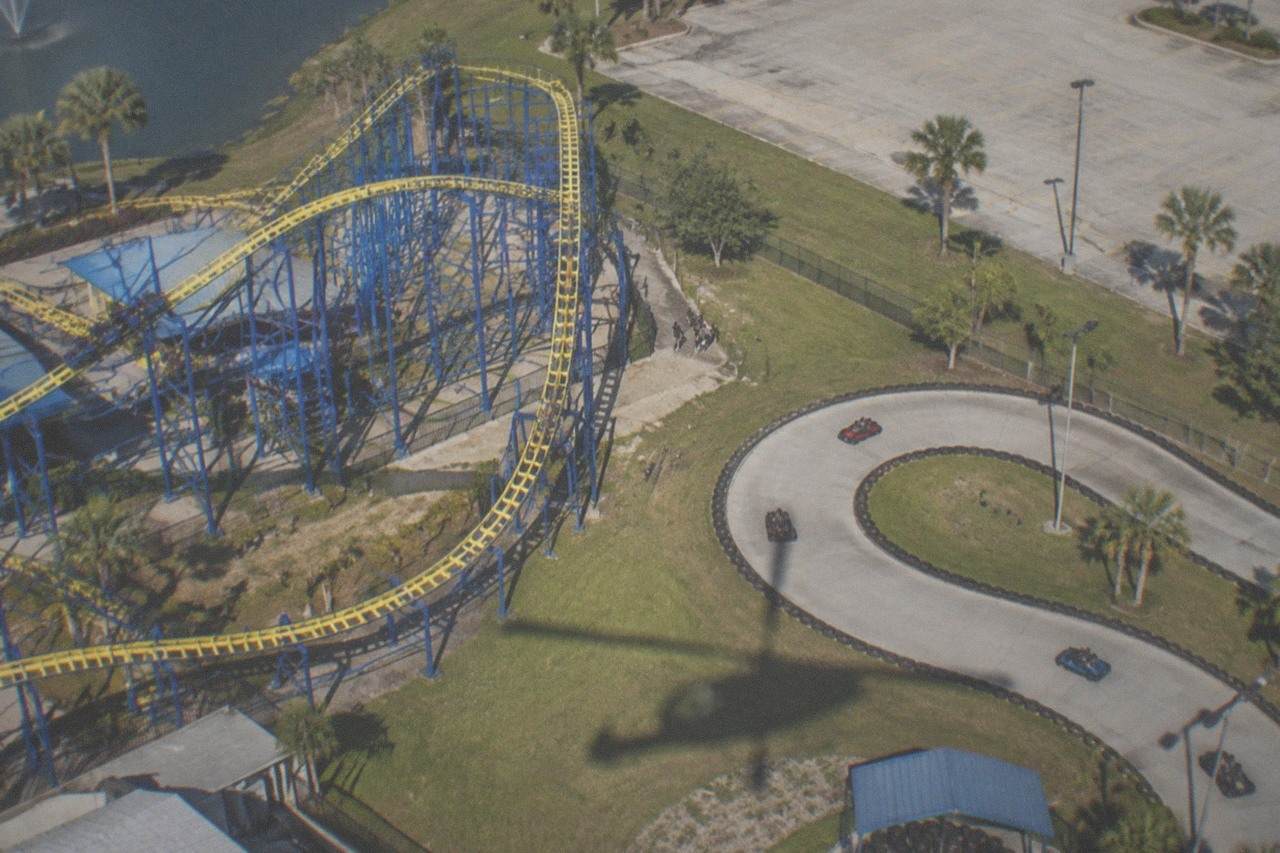 Aerial view of a small amusement park with go kart tracks and roller coasters beside a highway corridor
