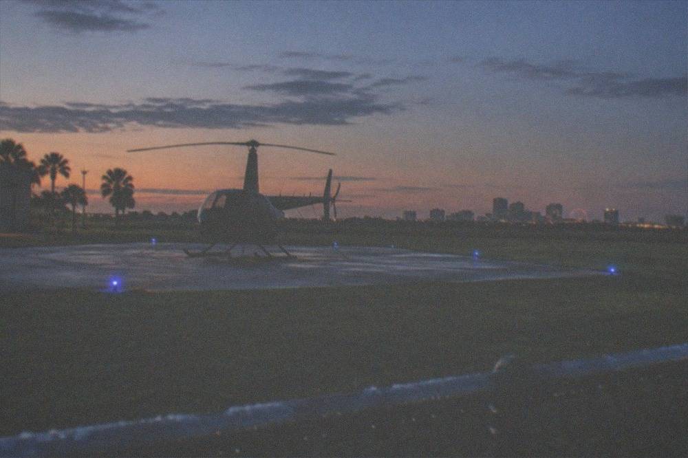 A lit helicopter pad at dusk with city lights on the horizon