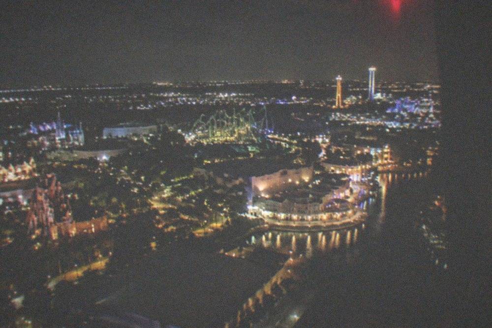Nighttime aerial view of a lit Florida theme-park corridor with glowing roads and distant park skylines