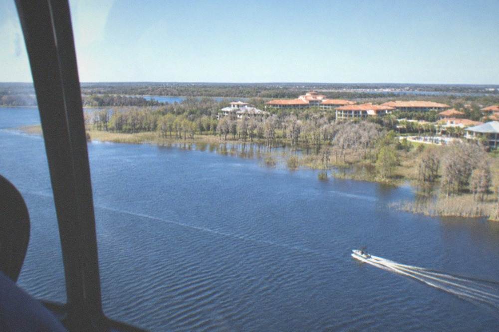 A helicopter flying over Florida lakes and resort rooftops under a clear dry-season sky