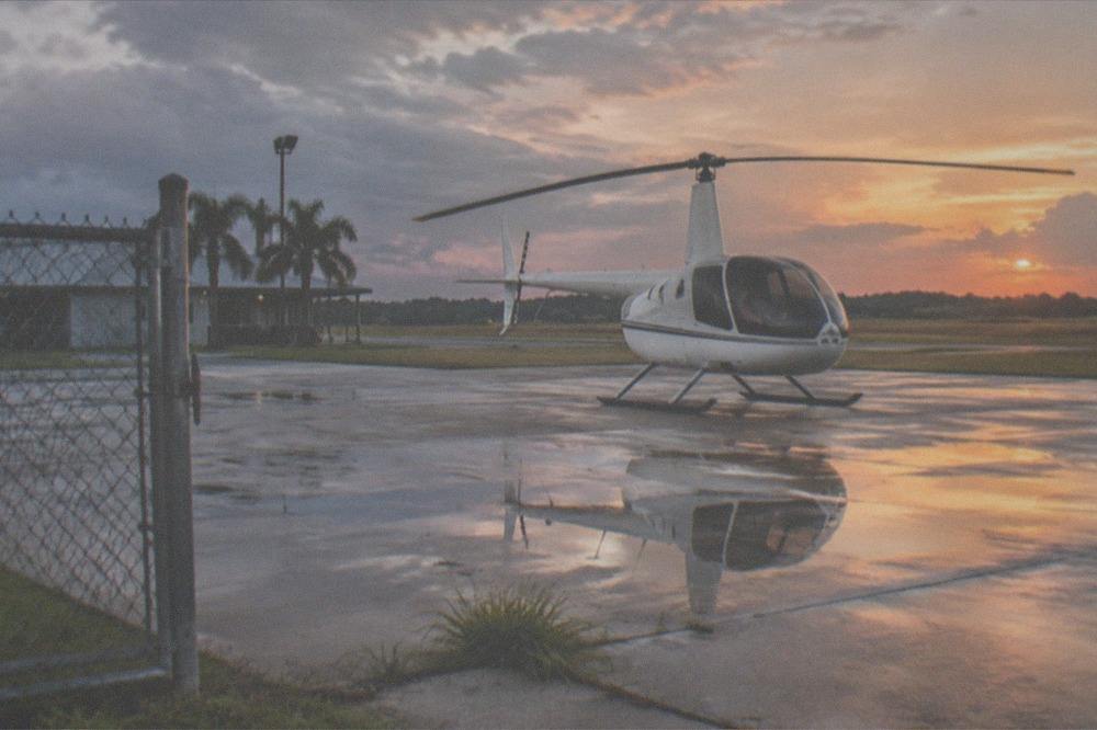 A tour helicopter parked at a Kissimmee helipad in warm evening light with a boarding area beside it