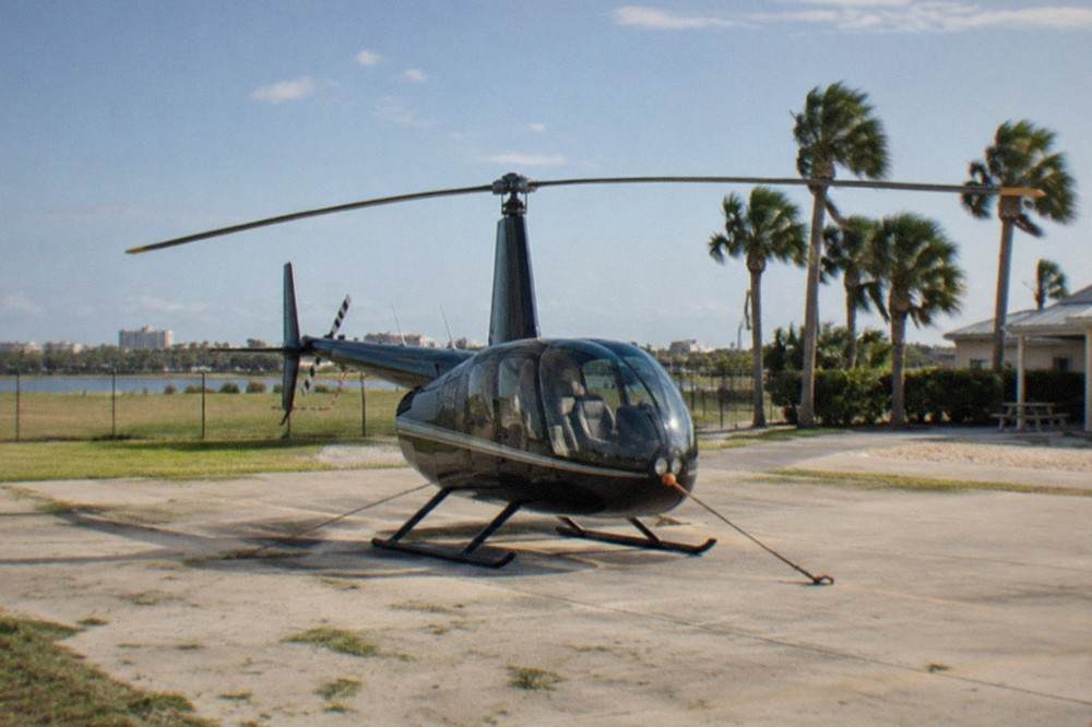 Robinson helicopter parked on a Kissimmee helipad with palm trees and open sky