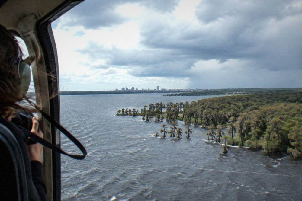 Open helicopter doorframe view over ocean coastline with dramatic clouds