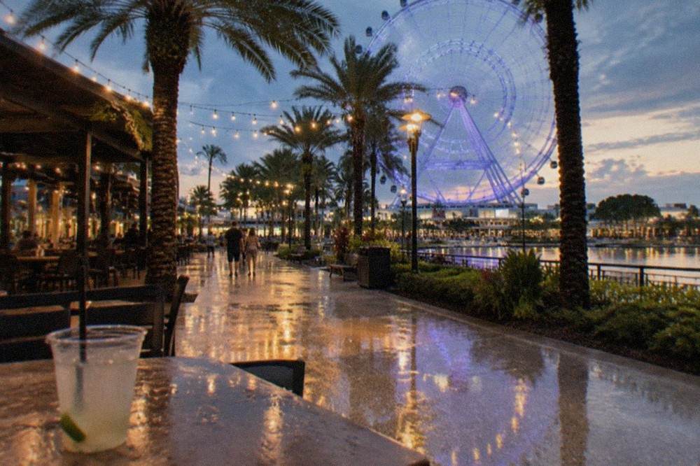 A waterfront entertainment district with string lights, palm trees and outdoor seating areas in the evening