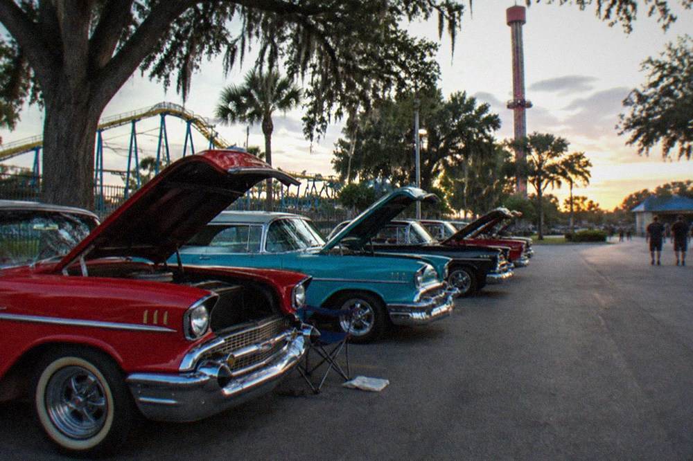 Vintage cars lined up on a tree-lined street at an outdoor entertainment district