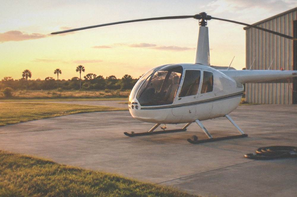 A small airport apron at golden hour with a helicopter parked beside a hangar