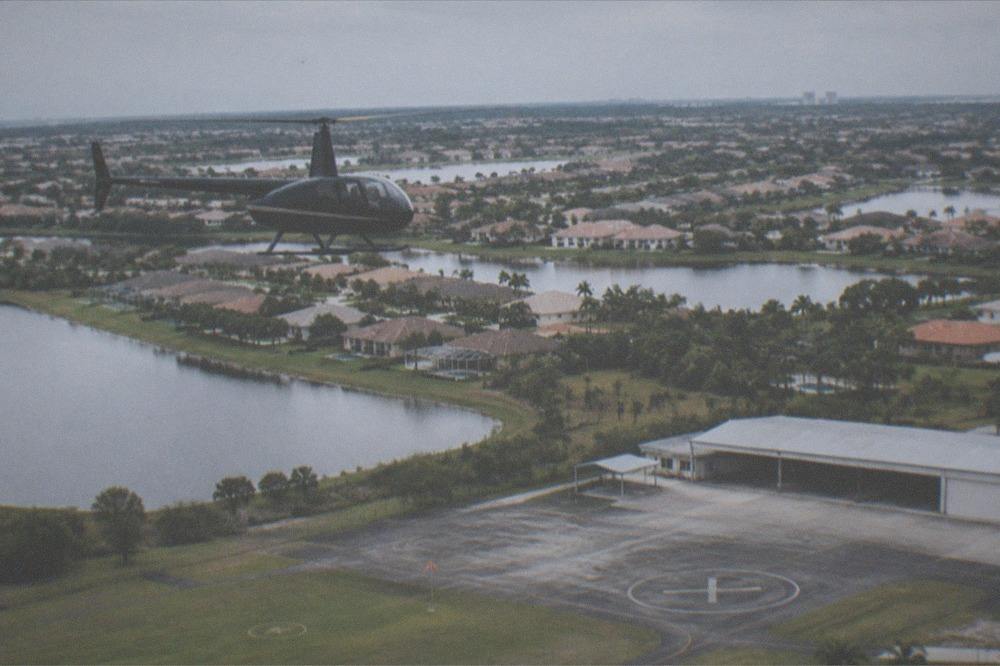 A helicopter flying over a sunlit suburban corridor with lakes and tree lines