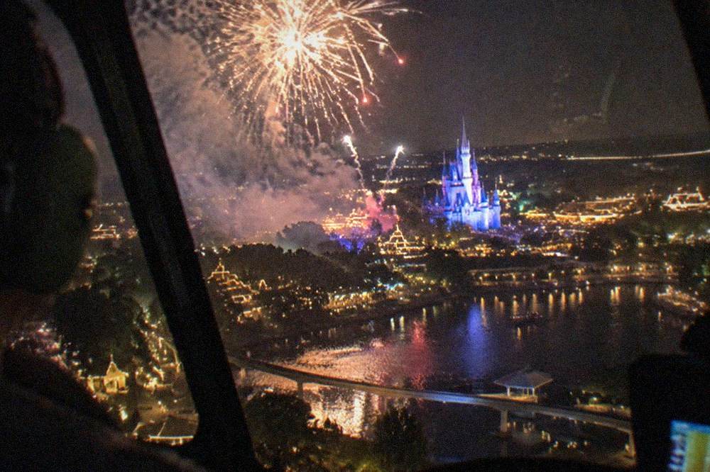 Theme park fireworks bursting over a dark horizon seen from the air