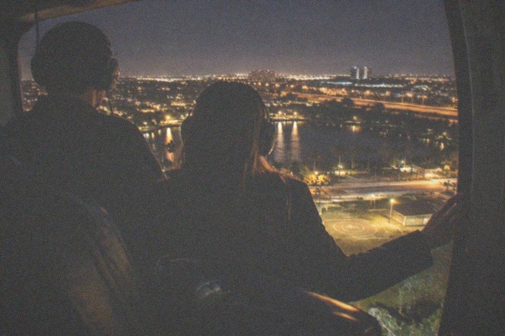 A couple silhouetted inside a helicopter cabin above city lights