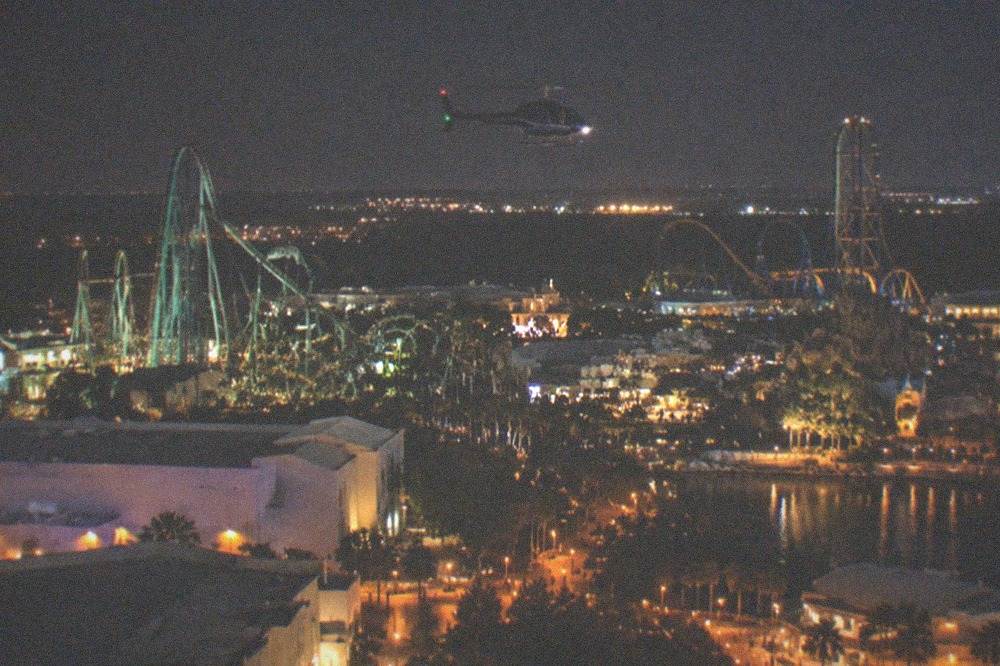 A helicopter in flight above the illuminated Orlando theme park corridor at night