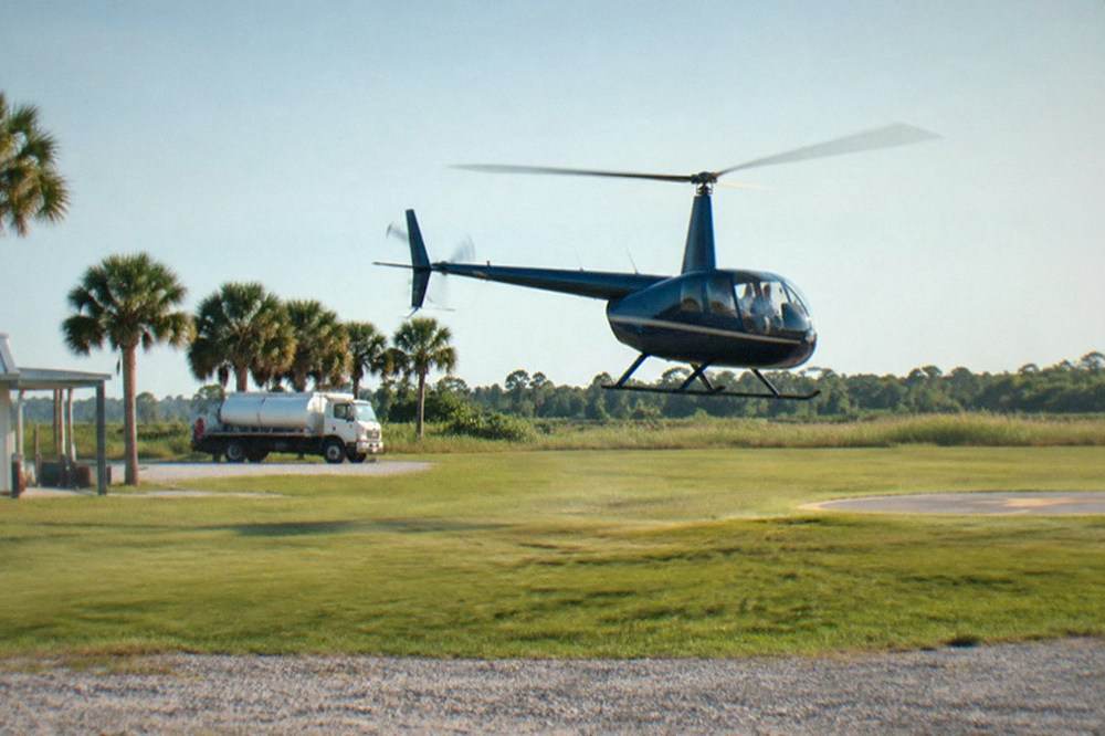 A small sightseeing helicopter lifting off from a grassy helipad in bright morning light