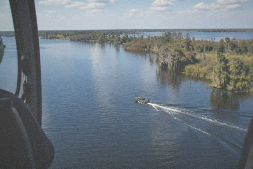 A helicopter flying over lakes and wooded Florida terrain under scattered white clouds