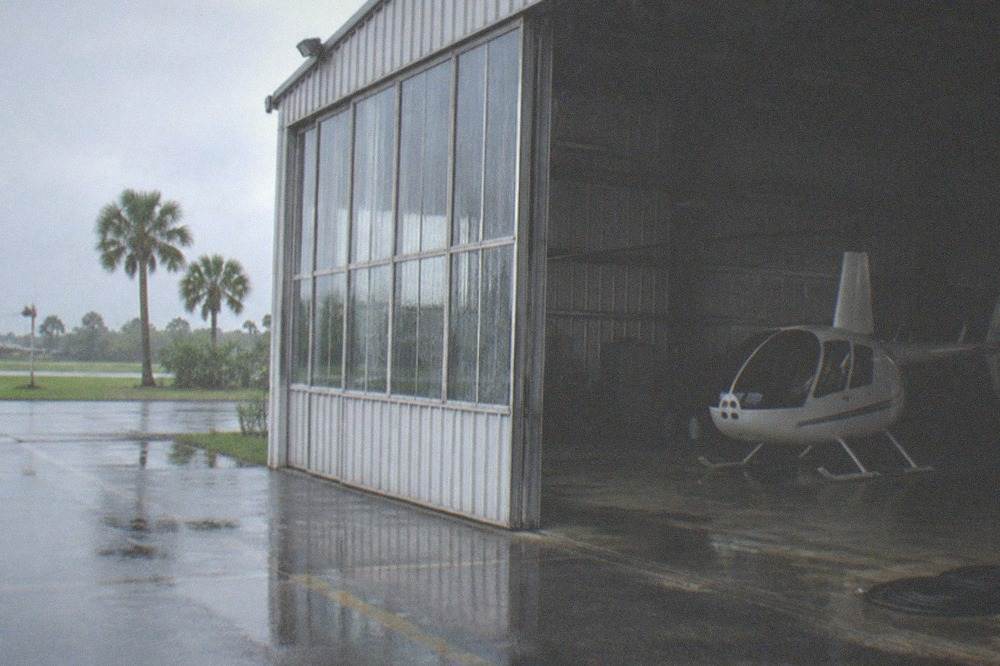 Rain falling on the windows of a helicopter hangar with a grounded aircraft visible inside