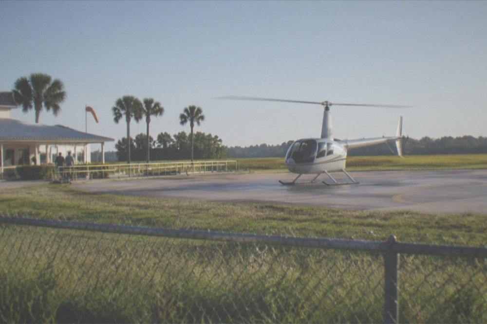 A calm Florida morning with clear skies over a helipad and a helicopter rotors turning