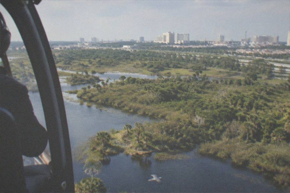 Helicopter in flight above Florida wetlands with a resort skyline in the distance