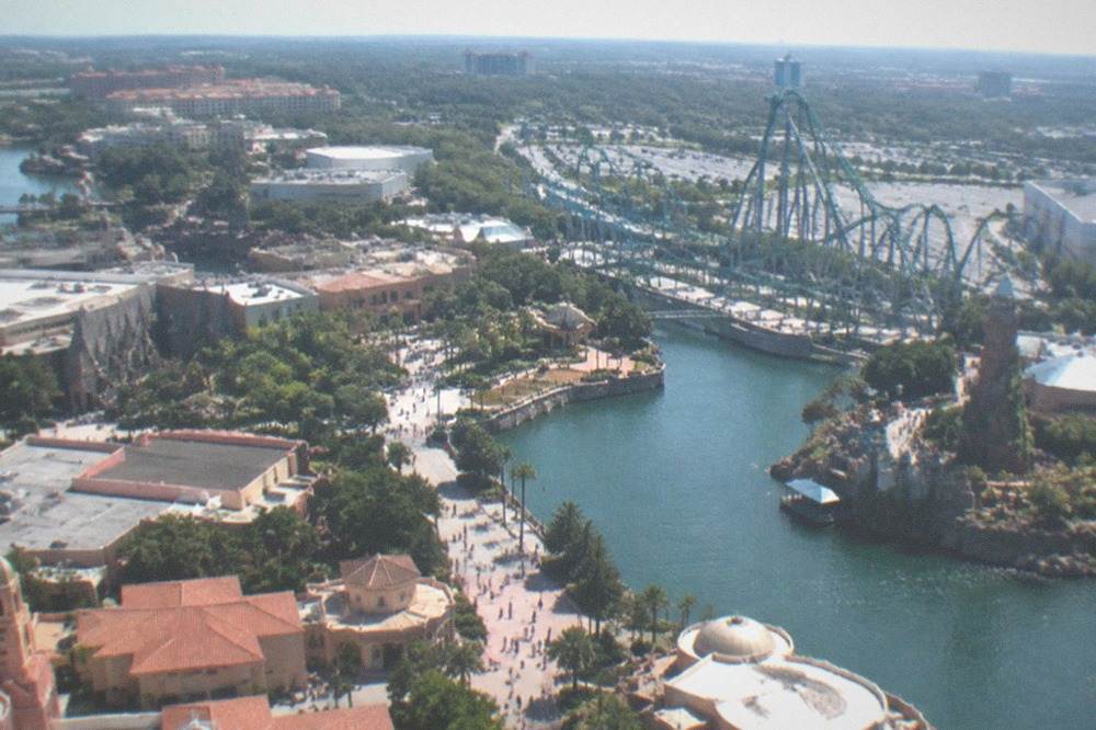 Aerial view of a Florida theme-park corridor with resort rooftops and tree-lined roads at midday