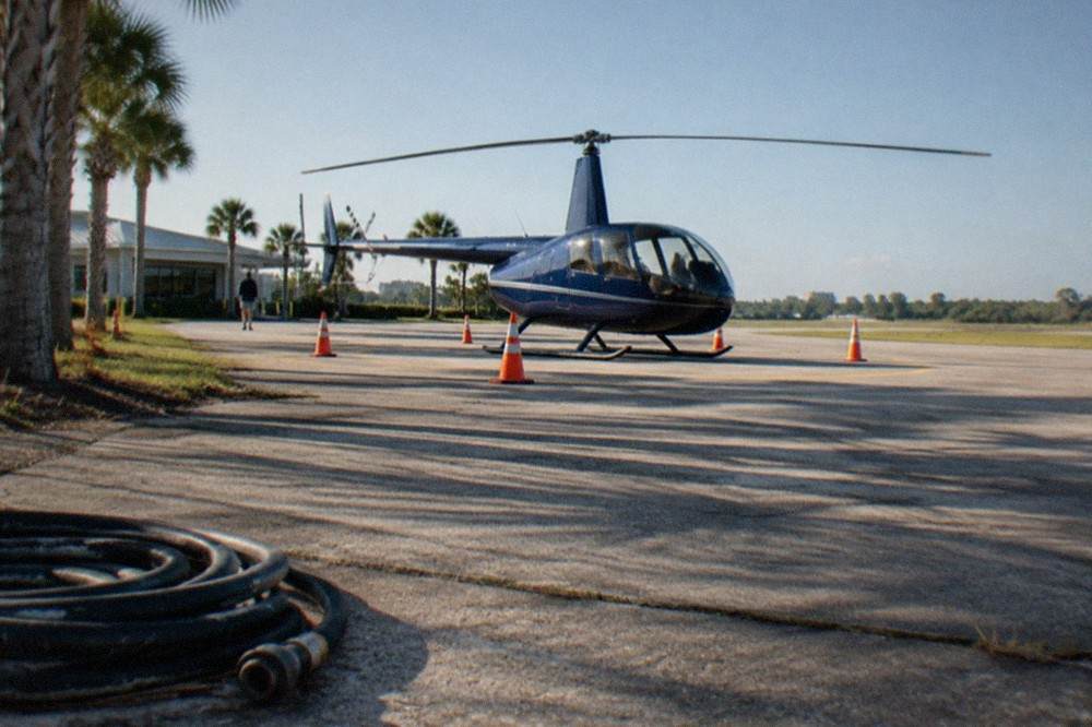 A four-seat sightseeing helicopter on a paved helipad with orange safety cones marking the landing area