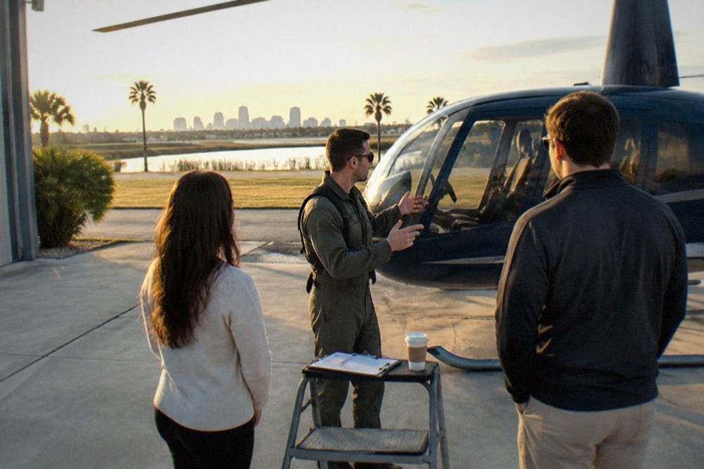 A pilot in a flight suit giving a pre-flight safety briefing to a small group beside a helicopter