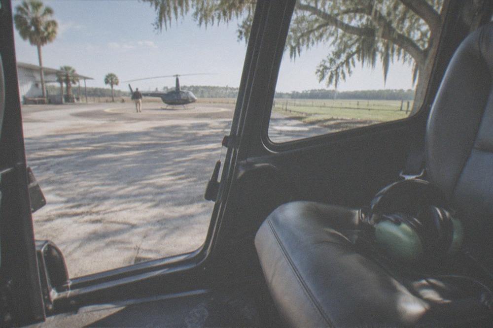 A small enclosed tour helicopter on the ground with large side windows and headset visible on a seat