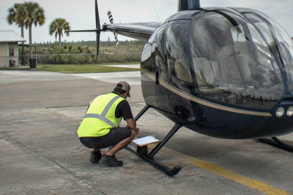 A tour crew member completing a pre-flight checklist beside a small helicopter