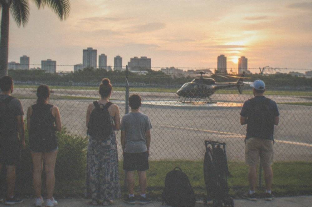 A group of travellers waiting at a Kissimmee helipad fence before a flight