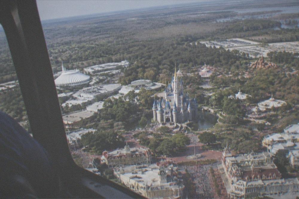 A small helicopter banking over a sunny Florida attractions corridor
