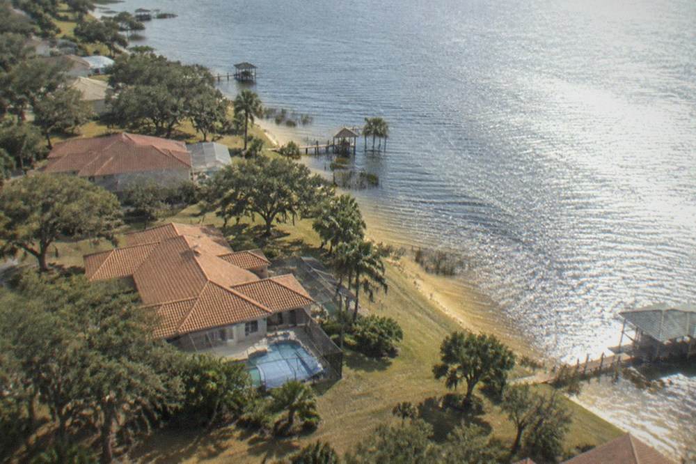 A helicopter in flight above a Florida lake with residential rooftops and greenery below