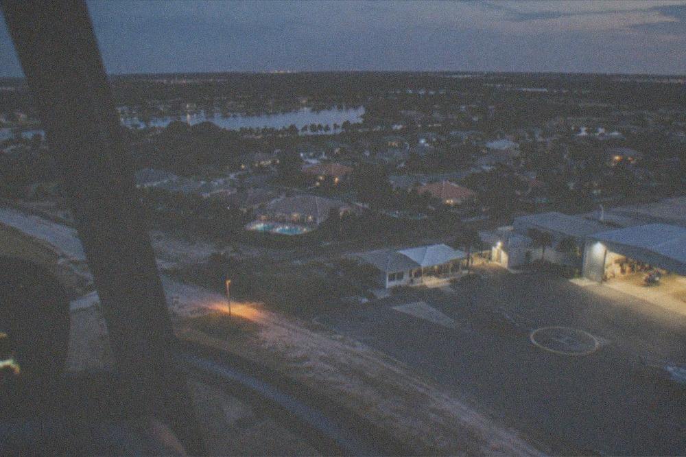 A helicopter flying at dusk above a Florida residential area with lights beginning to glow