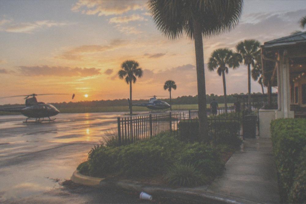 A Florida entertainment district street with palm trees, neon signs, and evening walkways
