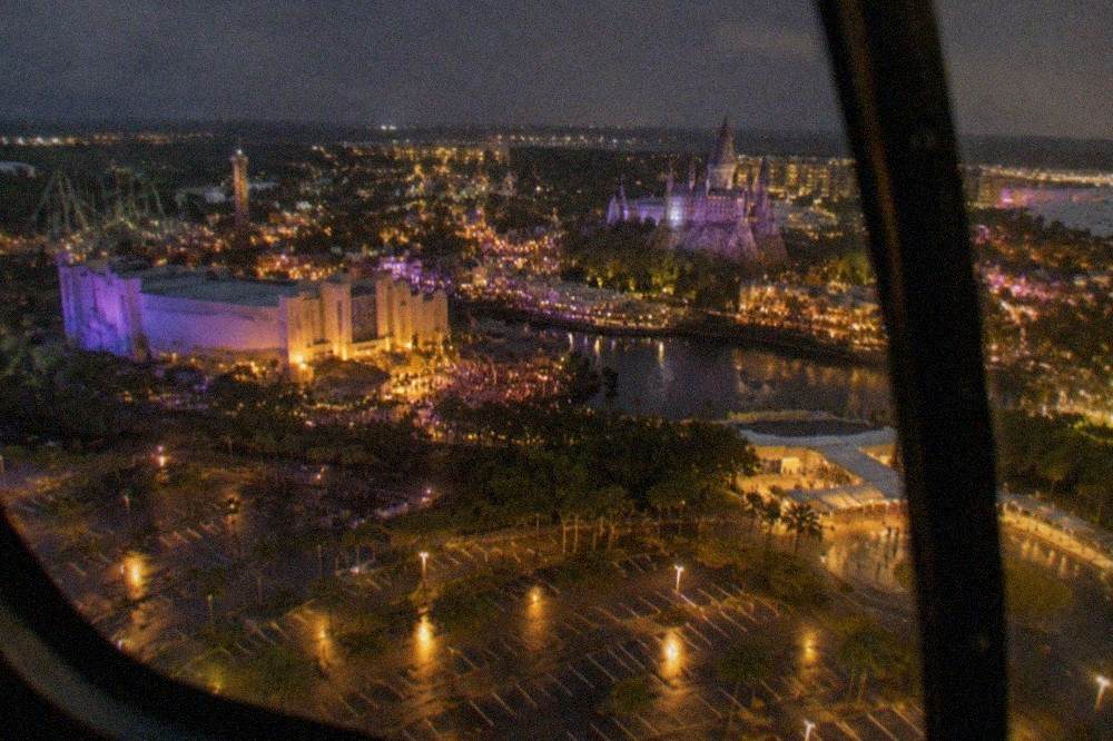 Aerial view of a brightly lit theme park resort area at night from a helicopter window