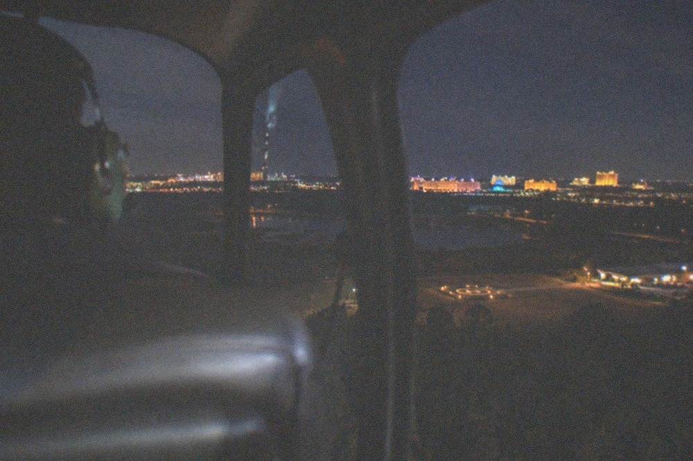 Helicopter interior at night with a window view of distant illuminated resort lights